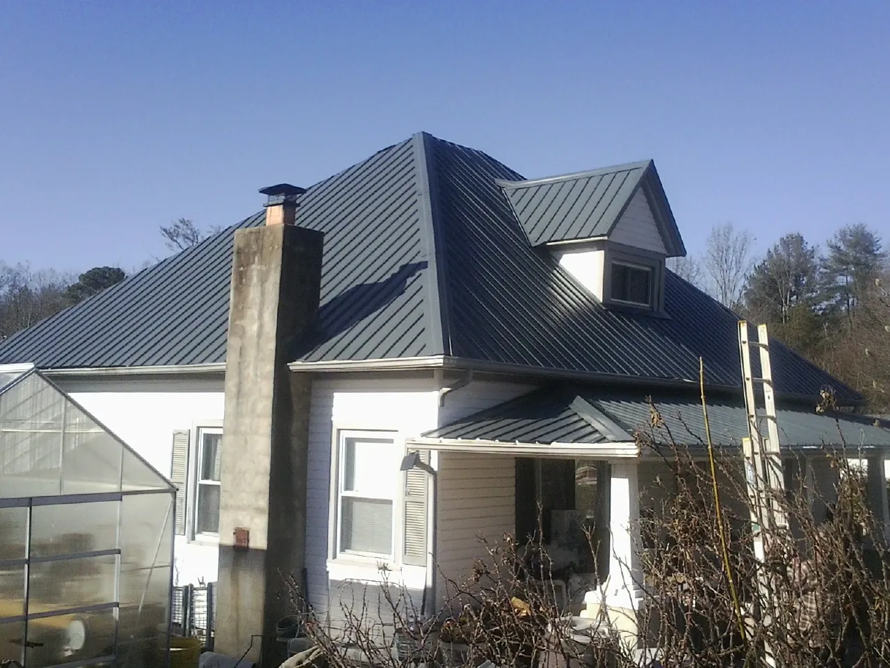 Dark blue standing seam metal roof on a white farmhouse with dormer — Slate & Tile Roof Repair by Roofing Brothers in Siler City