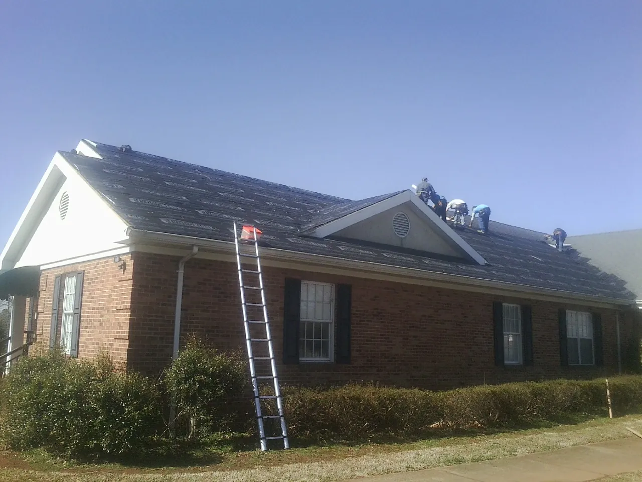 Crew tearing shingles off a brick ranch roof with a ladder set — Metal Roof Repair work by our crew in Siler City
