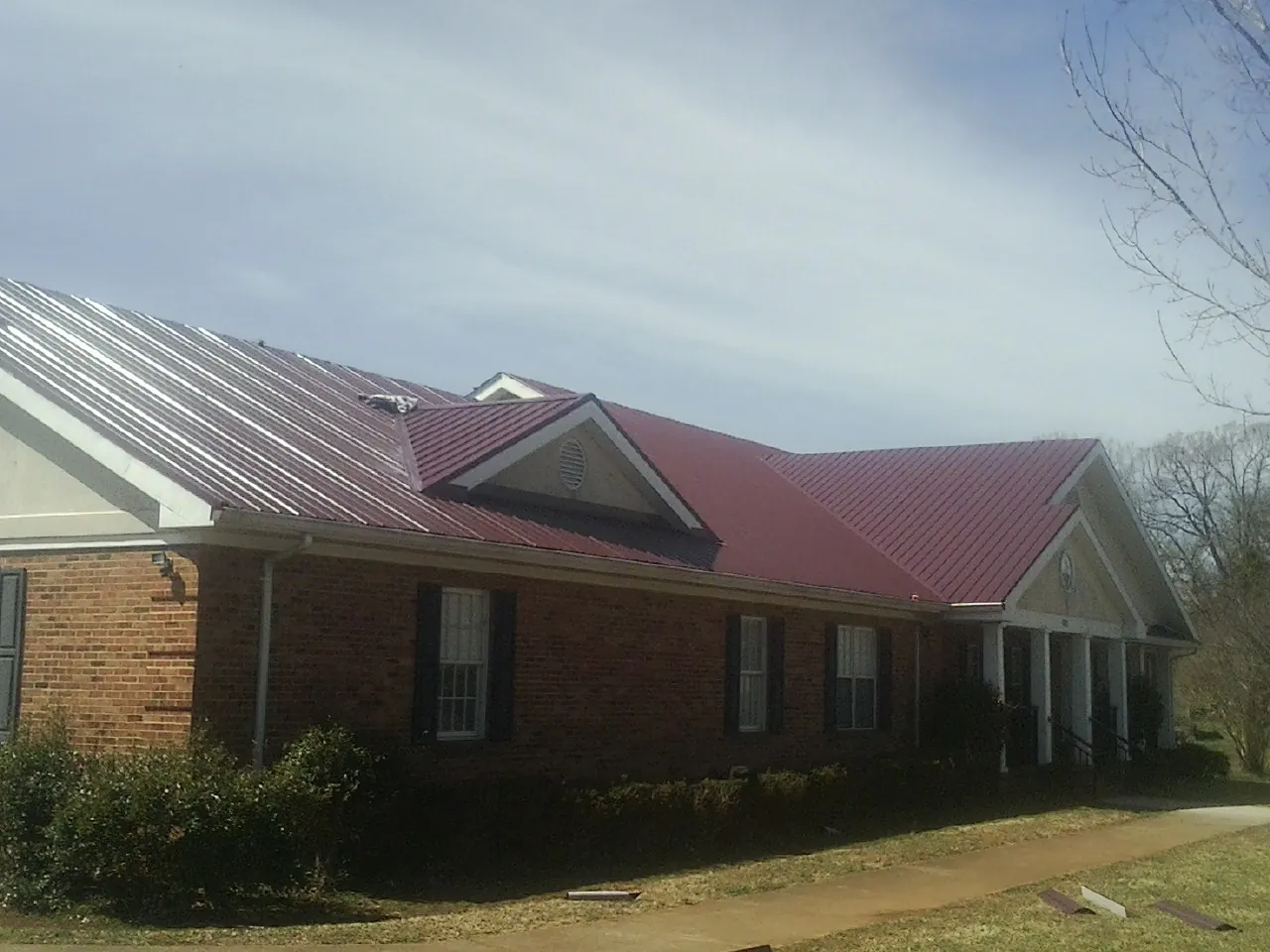 Red metal roof with gabled entries on a long brick building, from a Hail Damage Roof Repair job in Siler City