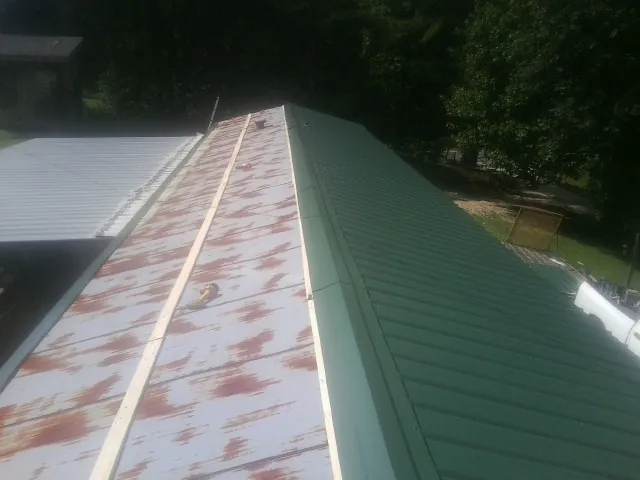 Old rusted panels beside newly installed green metal roofing — Wind Damage Roof Repair by Roofing Brothers in Siler City
