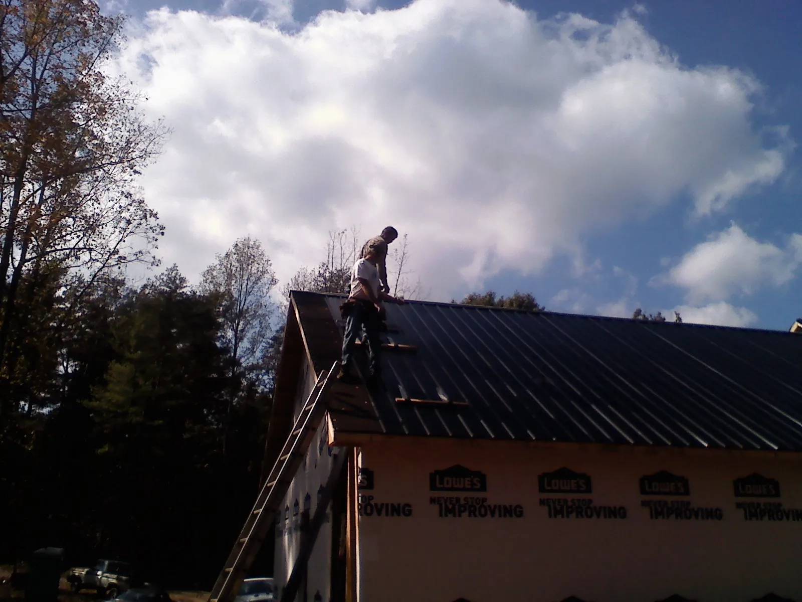 Roofer fastening dark metal panels high against a cloudy sky, from a Roof Inspection job in Siler City