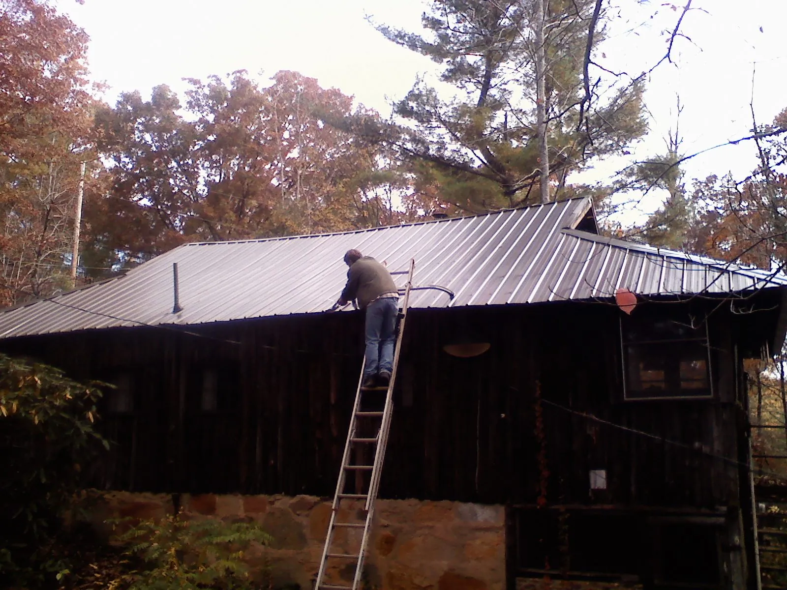 Roofer on a ladder working along the edge of a cabin metal roof in Siler City