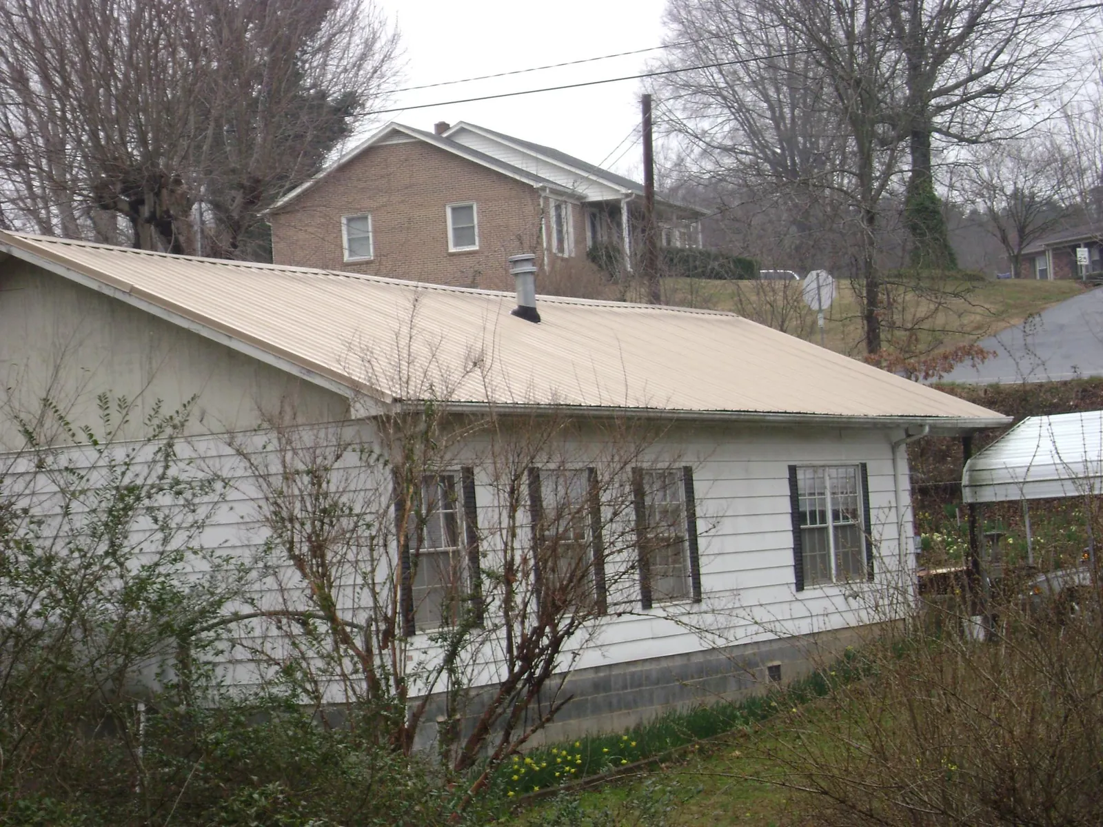 Tan metal roof on a white sided house set into a hillside — Commercial Roofing by Roofing Brothers in Siler City
