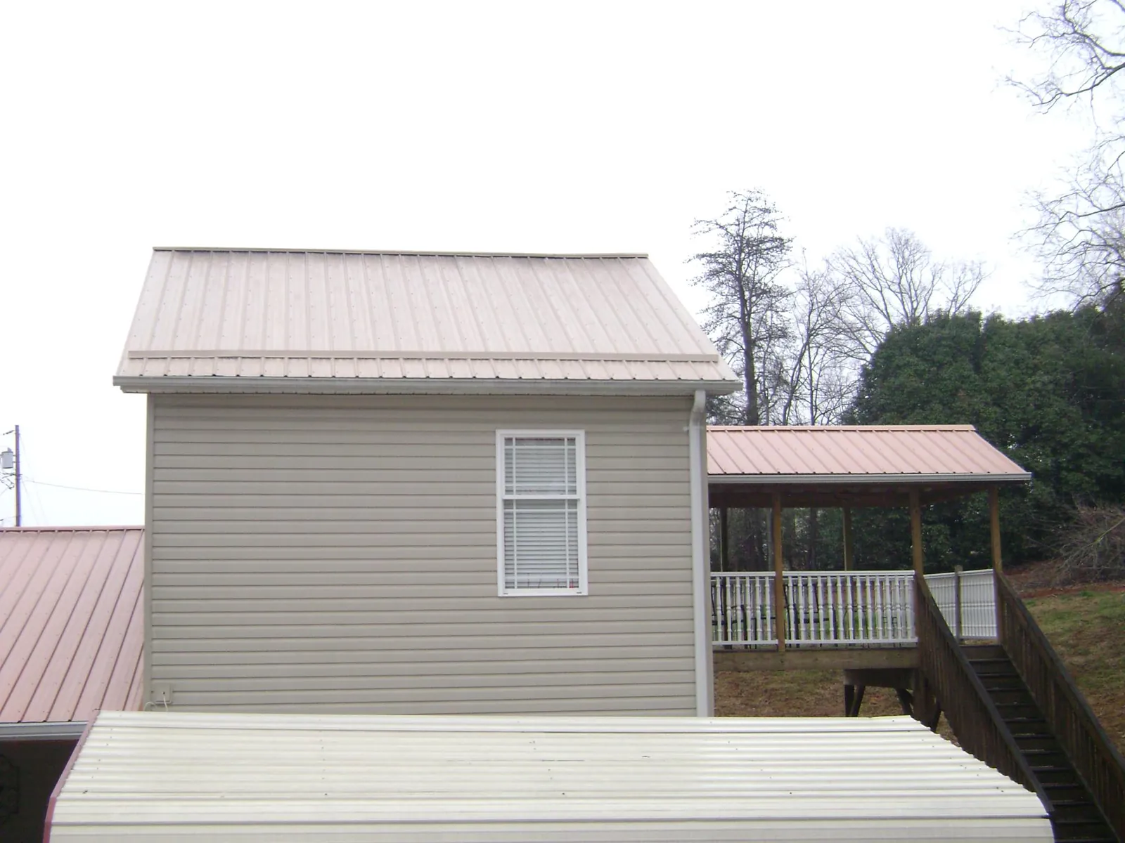 Tan metal roofs on a two story addition and attached porch, from a Roof Replacement job in Siler City